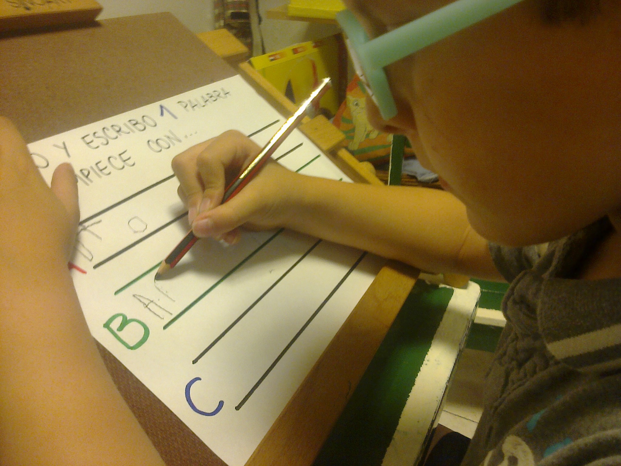 alumna del grupo  escribiendo palabras usando un atril y una hoja con renglones grandes